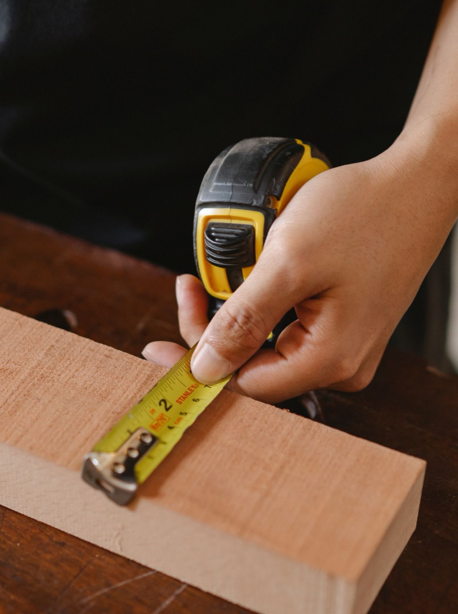 A hand holding a tape measure against a block of wood